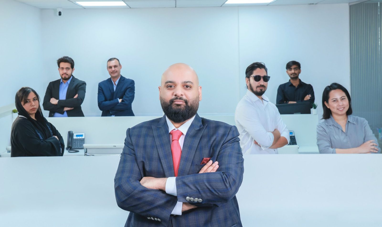 Professional business team standing confidently in a modern office with leader in front wearing suit and red tie.